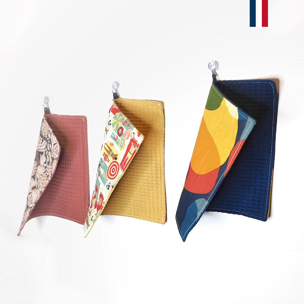 Vue de côté de trois essuie-tout réutilisables en tissu de couleurs rose, jaune et bleu. Le drapeau français apparaît en haut à droite de la photo.
